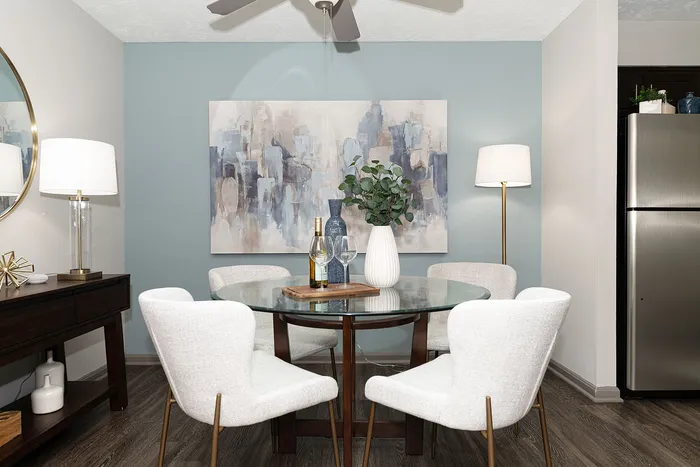 Chic dining area with modern glass table, stylish white chairs, and elegant decor set against a soothing blue accent wall.