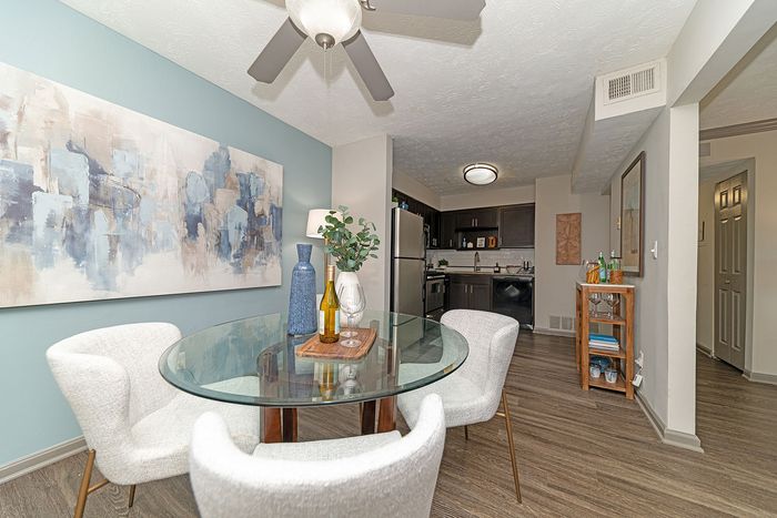 Modern dining area with elegant glass table, stylish chairs, and abstract wall art adjacent to a sleek kitchen with dark cabinetry and stainless steel appliances.