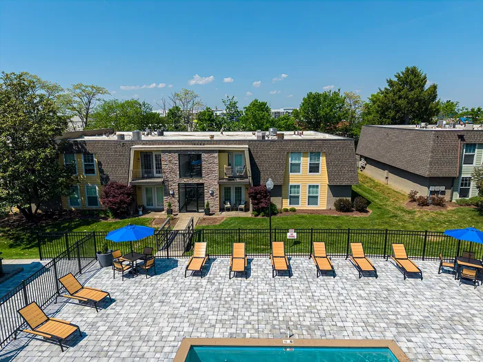 Inviting apartment complex featuring a pristine swimming pool, elegant sun loungers, and vibrant outdoor seating set against lush green landscaping.