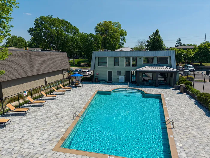 Inviting outdoor pool area with modern lounge chairs and a clubhouse, surrounded by lush greenery and a blue sky backdrop.
