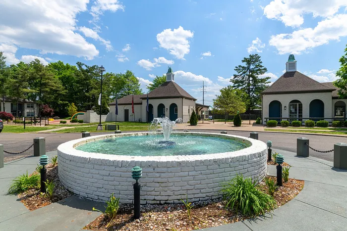 Charming community entrance with a scenic fountain, surrounded by elegant architecture and lush greenery under a bright blue sky.