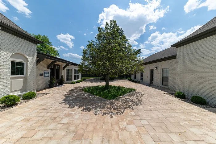 Charming courtyard with elegant stone pavers and lush greenery, framed by classic white brick homes under a bright blue sky.