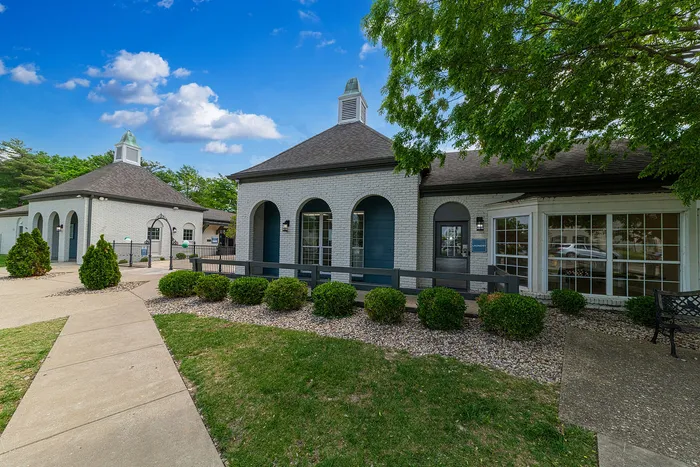 Charming apartment complex exterior featuring arched windows, manicured landscaping, and a tranquil pathway under a clear blue sky.
