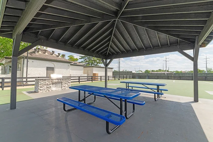 Inviting outdoor gazebo area featuring modern picnic tables and a stylish stone grill, perfect for gatherings and leisure activities.
