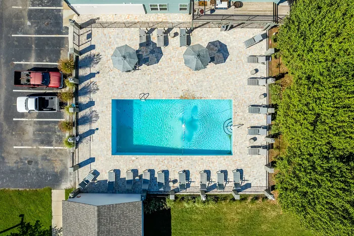 Luxurious aerial view of a sparkling swimming pool with sun loungers and umbrellas, surrounded by lush greenery and convenient parking.