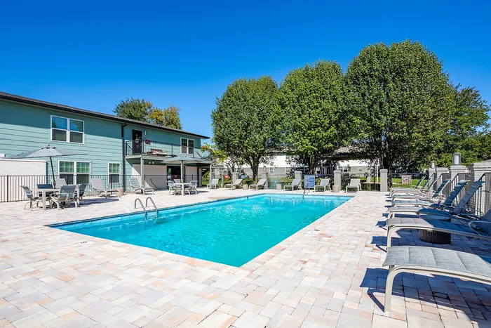 Inviting outdoor pool area with stylish lounge chairs, surrounded by lush trees and modern apartment building.