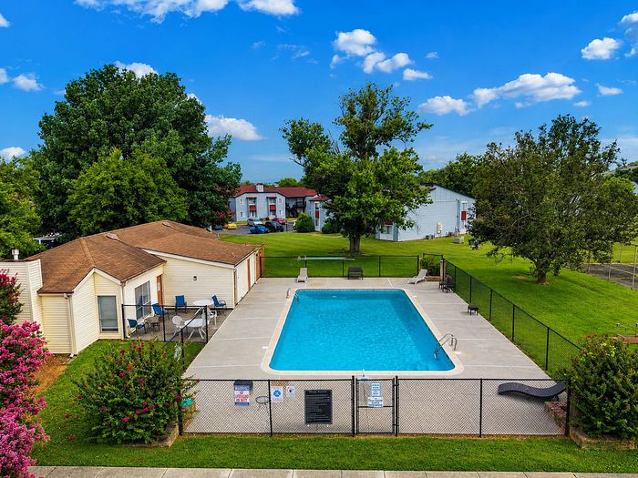 Inviting community pool with surrounding lush green landscape and cozy residential buildings, perfect for relaxation and leisure.