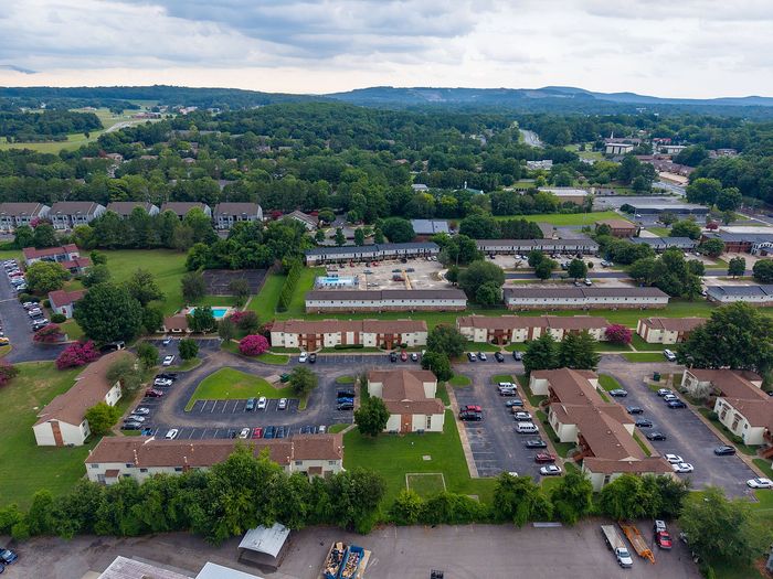 Scenic aerial view of a vibrant apartment complex nestled in lush greenery with ample parking and recreational amenities.