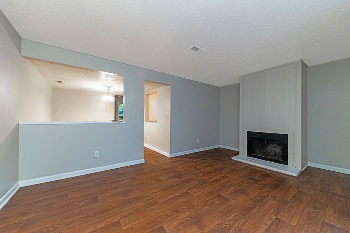 Elegant living room with rich wooden floors, modern fireplace, and open design leading to a well-lit dining area.