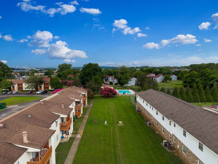 Inviting apartment complex with charming balconies, lush green surroundings, and a sparkling pool under a bright blue sky.