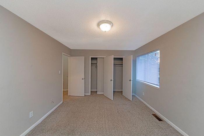 Spacious bedroom with neutral tones, featuring dual closets and a large window for natural light.