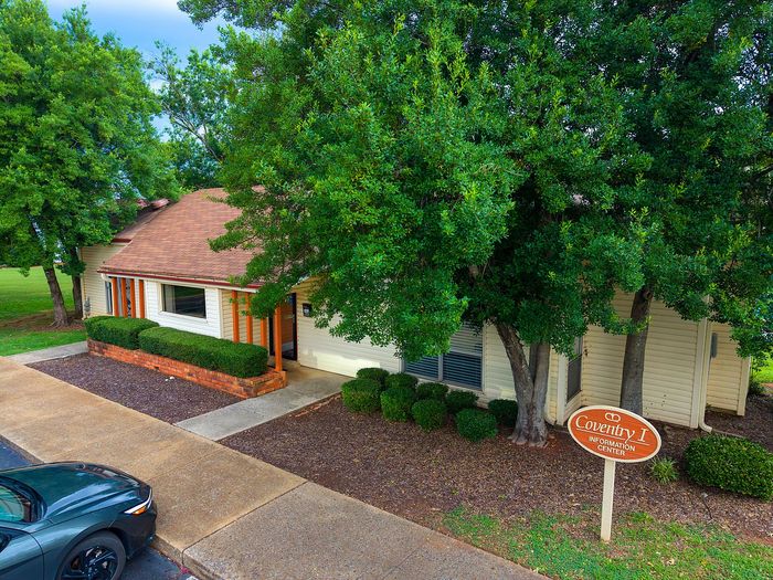 Charming residential building nestled among lush trees, featuring a welcoming entrance with a neatly landscaped path and an inviting information center.