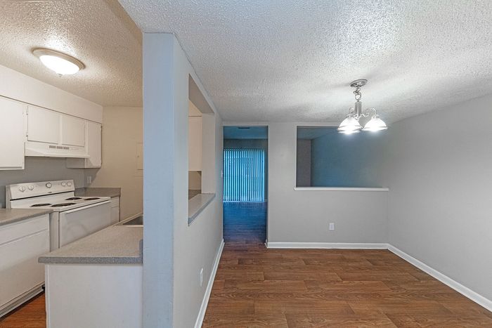 Inviting open-plan living area with stylish hardwood floors, bright kitchen, and elegant chandelier lighting.