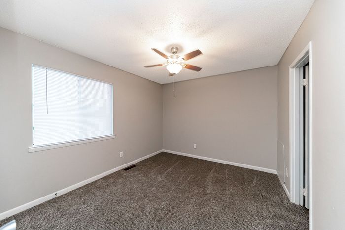 Bright and spacious bedroom with plush carpeting and a ceiling fan, perfect for comfort and relaxation.