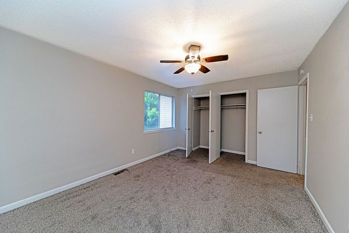 Spacious bedroom with plush carpeting, modern ceiling fan, and ample closet space, perfect for comfort and organization.
