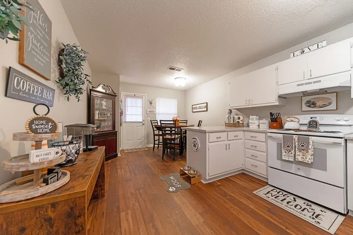 Charming kitchen with warm wooden floors, white cabinetry, and cozy dining area, enhanced by delightful home decor accents and natural light.