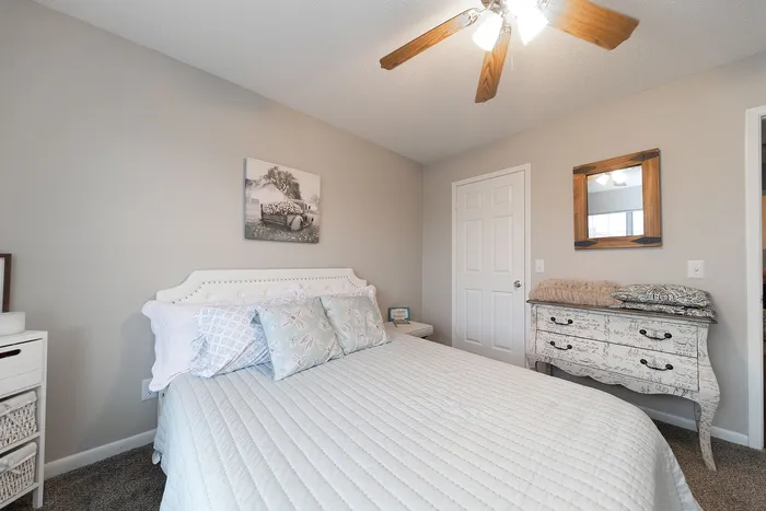 Inviting bedroom with elegant decor, featuring a cozy white bed with patterned pillows, a chic dresser, and warm ambient lighting.