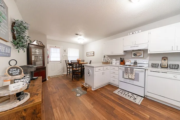 Charming kitchen with elegant wooden floors, crisp white cabinetry, and cozy dining area, perfect for welcoming warmth and style into your home.