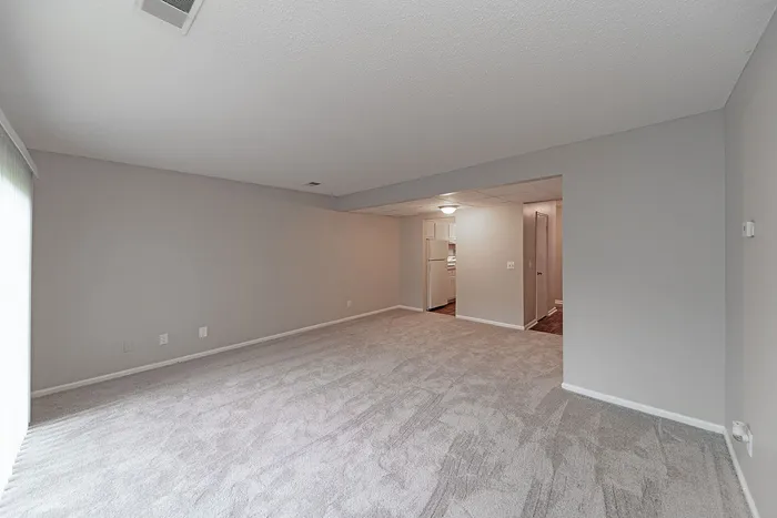 Spacious living area with plush carpeting and a view into a bright kitchen. Ideal for comfortable modern living.