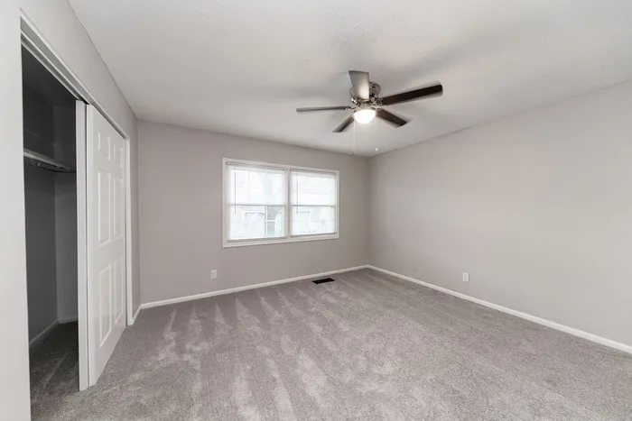 Bright, spacious bedroom with plush carpet and modern ceiling fan, featuring ample natural light from large windows.