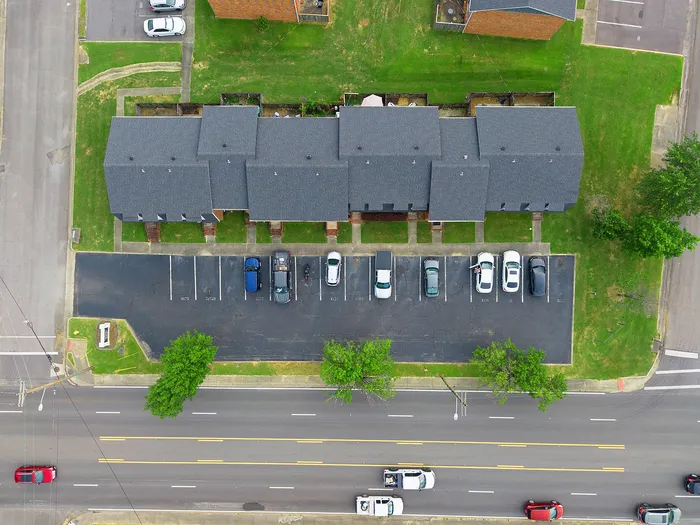 Aerial view of modern townhouses with adjacent parking area, surrounded by lush green lawns and a well-maintained street.