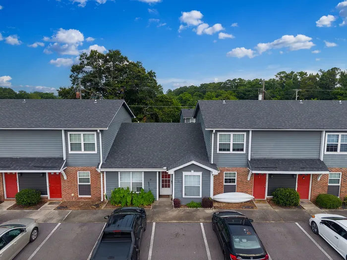 Charming townhouses with distinctive red doors, ample parking, and lush greenery under a vibrant blue sky.