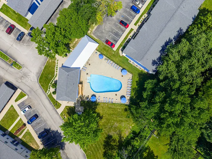 Aerial view of a vibrant apartment complex featuring a sparkling pool with sun loungers, surrounded by lush greenery and ample parking space.