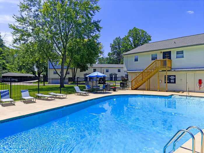 Inviting outdoor pool area with comfortable lounge chairs, surrounded by lush greenery and charming residential buildings.