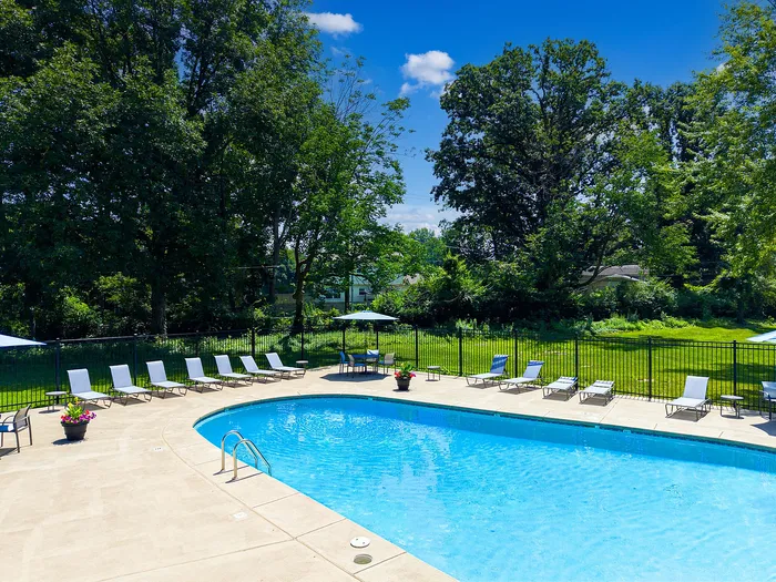 Inviting outdoor swimming pool area with sun loungers and surrounding lush green scenery, perfect for relaxation under a clear blue sky.
