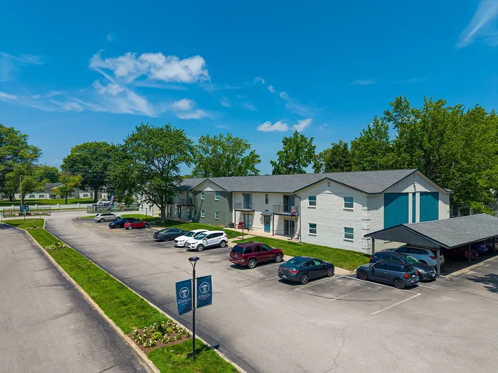 Charming apartment complex with spacious parking, surrounded by lush greenery under a clear blue sky.