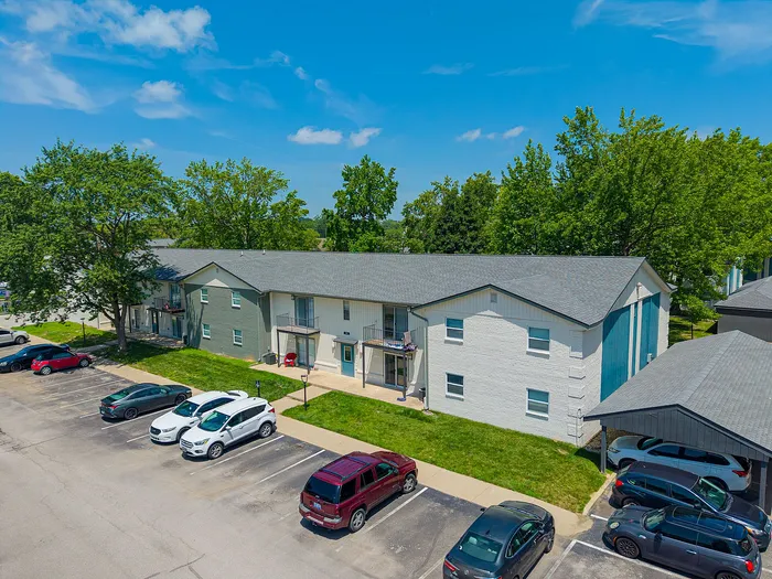 Charming apartment complex surrounded by lush greenery and bright blue skies, featuring ample parking and a peaceful residential ambiance.