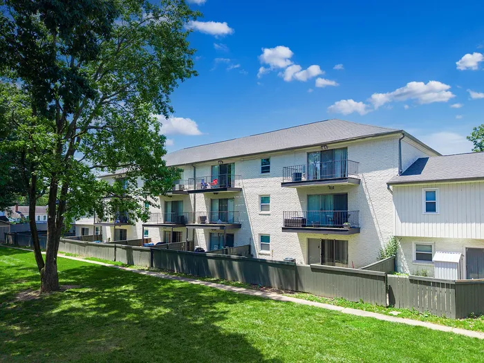 Charming apartment building with private balconies and lush green surroundings under a clear blue sky.