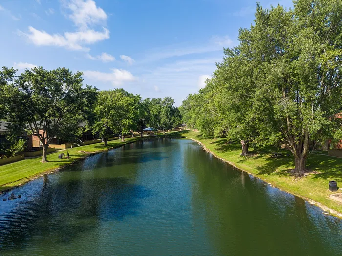 Scenic view of a serene lake bordered by lush green trees and grassy banks, ideal for relaxation and outdoor enjoyment.
