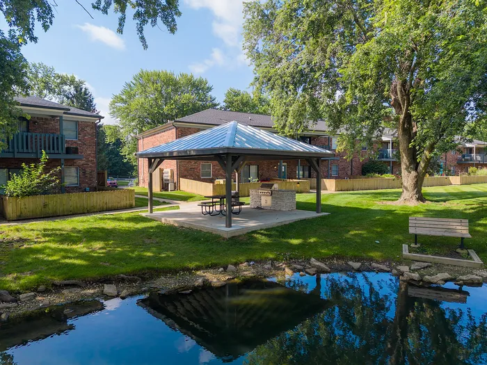 Charming apartment complex with serene outdoor pavilion, lush greenery, and tranquil pond views.