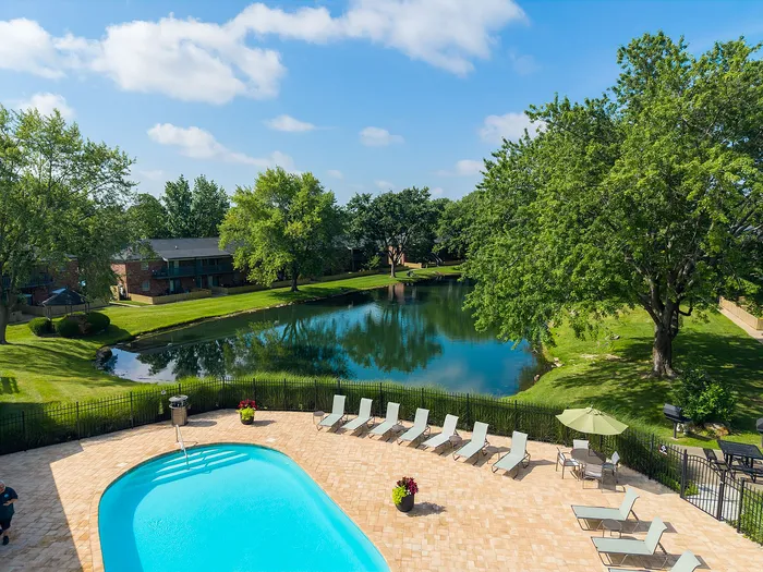 Stunning apartment view featuring a sparkling pool, lush greenery, and a serene pond, offering a perfect blend of relaxation and nature.