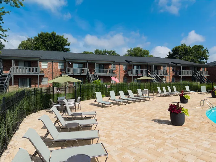 Inviting apartment complex with a sunlit pool area, surrounded by comfortable lounge chairs and vibrant greenery.