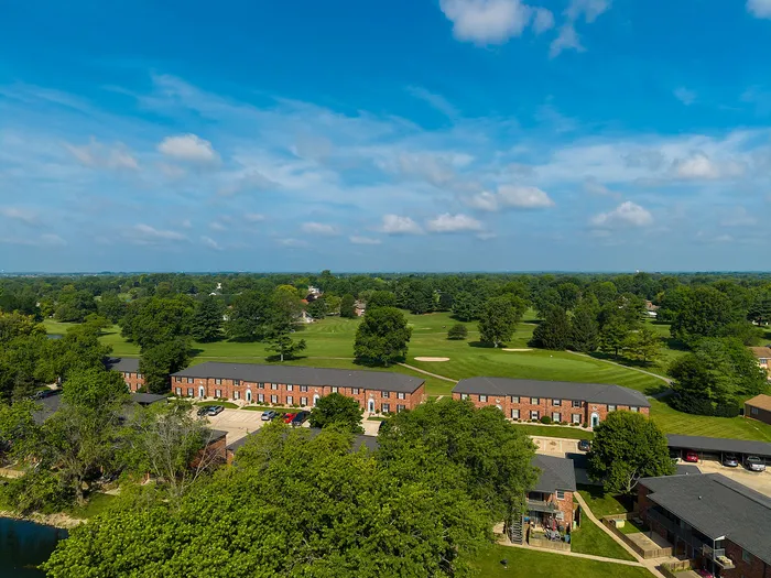 Scenic aerial view of charming brick apartment complex surrounded by lush greenery and a golf course under a vibrant blue sky.
