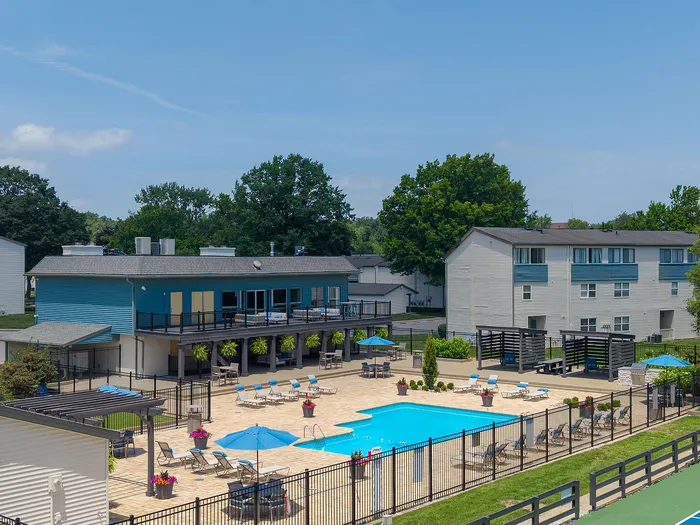 Inviting apartment complex with a sparkling swimming pool, sun loungers, and modern multi-story buildings surrounded by lush greenery.