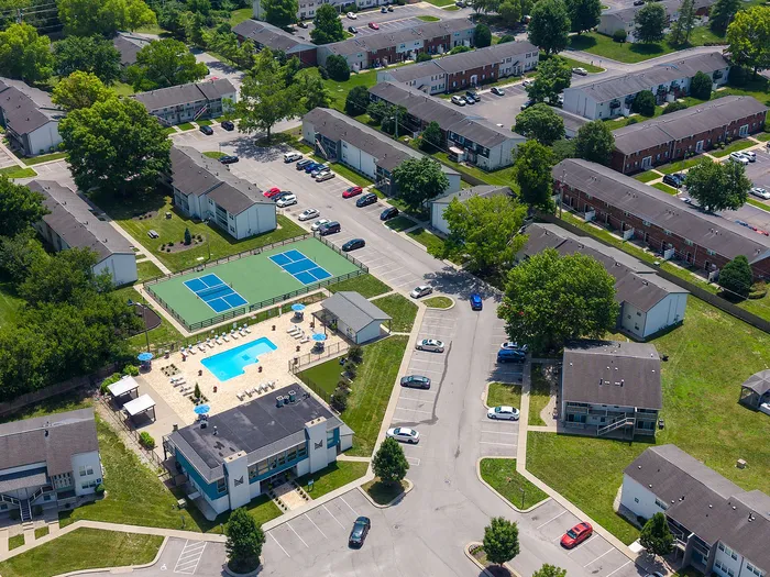 Vibrant aerial view of a residential complex featuring lush greenery, a beautifully maintained swimming pool area, and adjacent sports courts, offering a resort-style living atmosphere.
