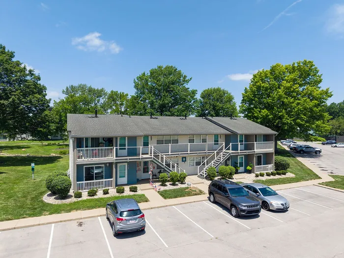Charming two-story apartment building with vibrant greenery, ample parking, and a sunny outdoor setting.