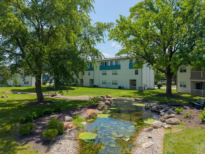 Charming apartment complex surrounded by lush greenery and a serene pond, creating a peaceful and inviting atmosphere.