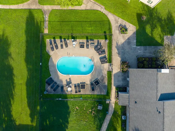 Aerial view of a luxurious outdoor swimming pool surrounded by lush green lawns and comfortable lounge chairs, perfect for relaxation.