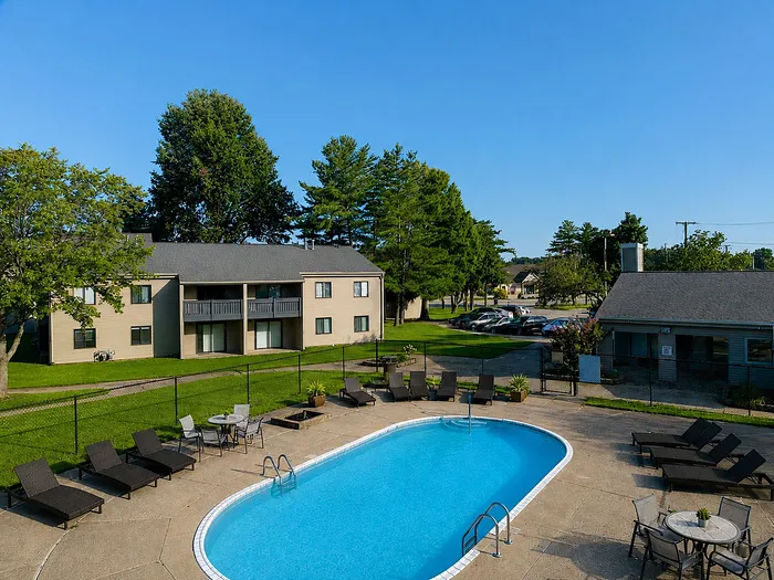 Inviting outdoor area with a sparkling pool surrounded by sun loungers, lush greenery, and charming apartment buildings, ideal for relaxation and leisure.