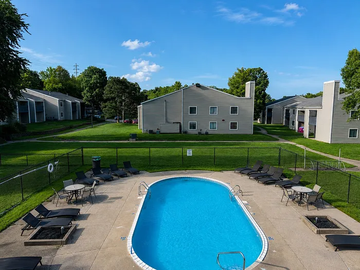 Inviting apartment complex with a refreshing outdoor pool, surrounded by lush green lawns and cozy seating areas, perfect for relaxation.