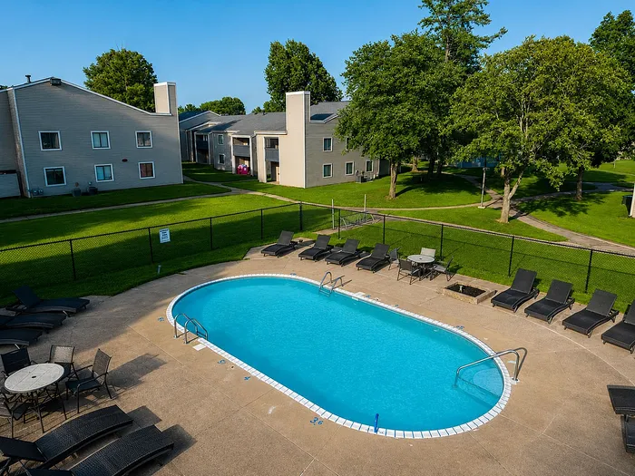 Inviting outdoor apartment pool area with modern lounge chairs and lush green surroundings.