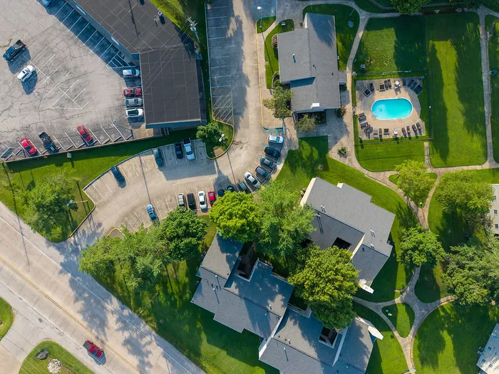 Aerial view of a serene apartment complex featuring buildings surrounded by lush greenery, ample parking, and a sparkling swimming pool.