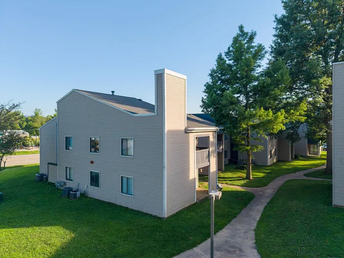 Charming apartment complex with modern exterior, surrounded by lush green lawns and shaded walkways.