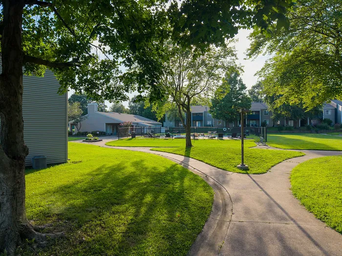 Charming apartment community with lush green lawns, winding pathways, and well-maintained common areas under a clear blue sky.