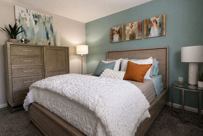 Elegant bedroom with textured white bedding, vibrant cushions, and modern decor in a serene setting.