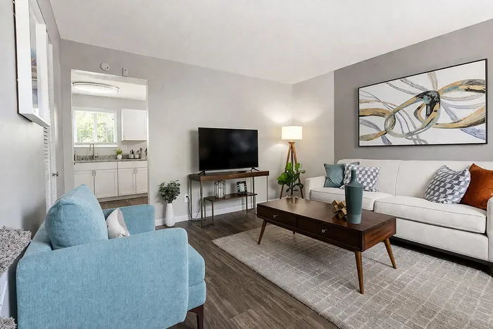 Chic living room featuring a modern white sofa, elegant wooden coffee table, and vibrant artwork, leading to a bright, open kitchen.